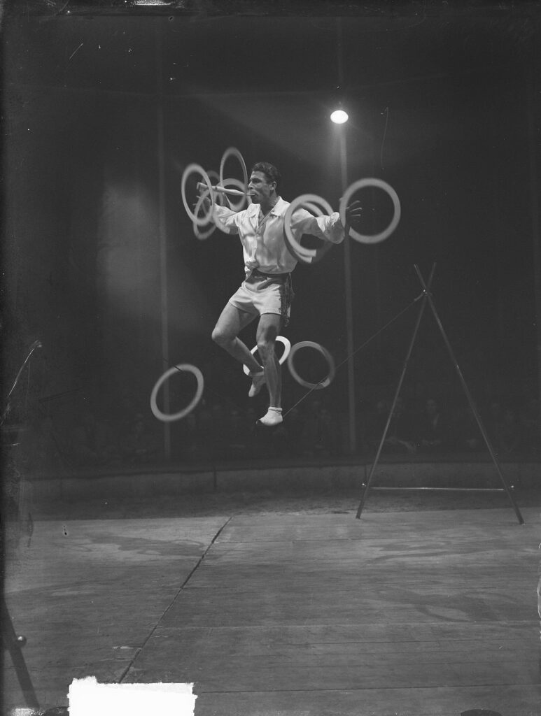 A man balancing on a rope, spinning round items on his arms.