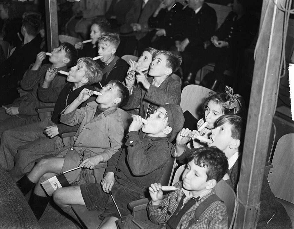 A crowd of children watching a show while eating a snack.