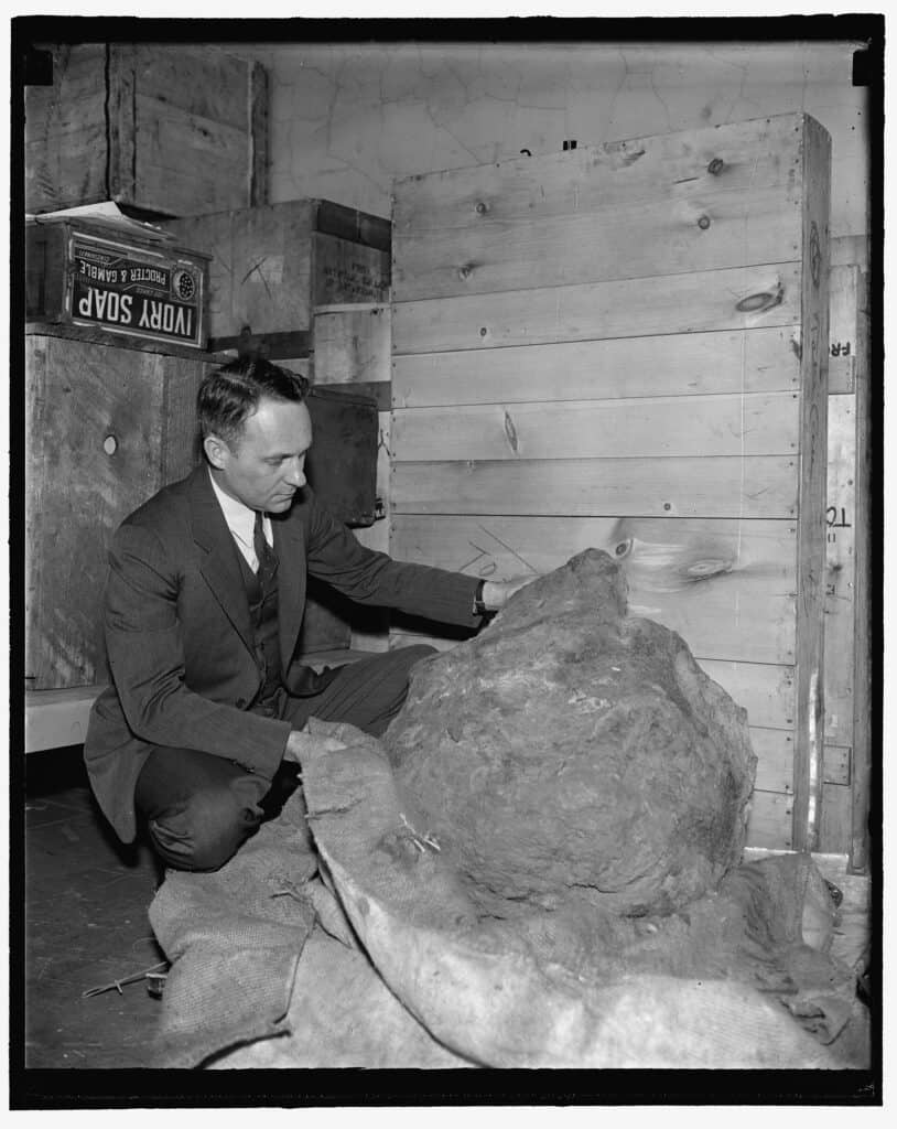 A man is kneeling next to a giant rock.