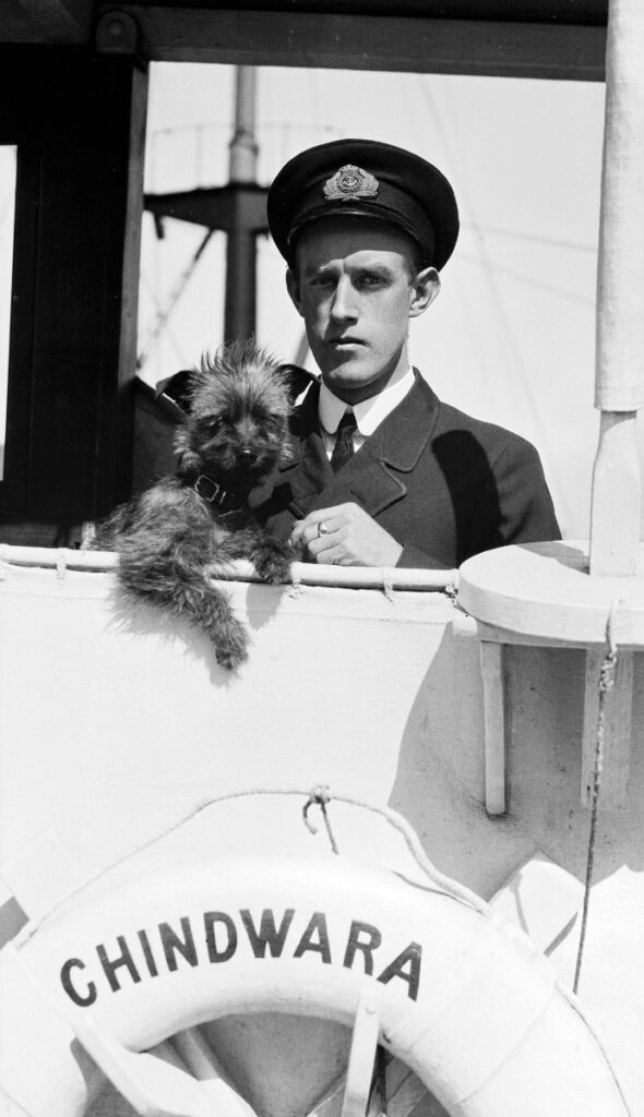 A uniformed man holding his small dog on a boat. 