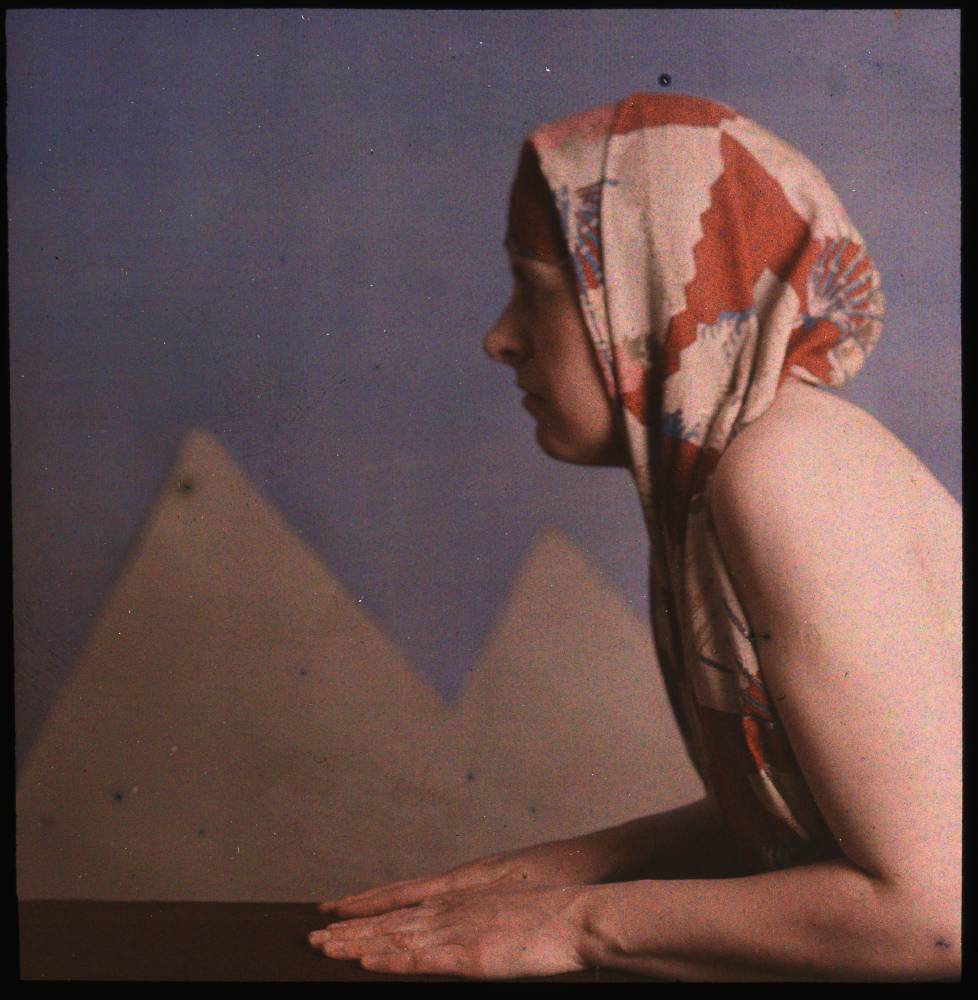 A Woman laying on the floor posed like a sphinx, in front of a fake poster of pyramids.